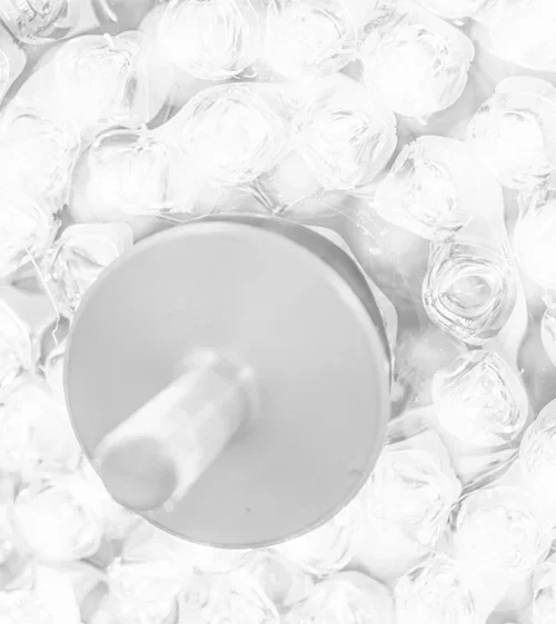 Highly blurred, monochromatic (white/light grey) close-up abstract image of ice cubes surrounding a white bottle or container.